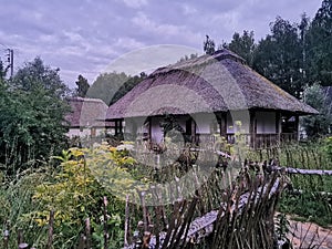 An old wooden Ukrainian hut on a farm in the evening, cloudy sky