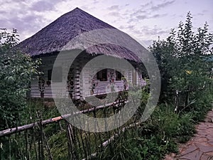 An old wooden Ukrainian hut on a farm in the evening, cloudy sky