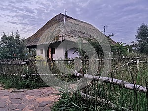 An old wooden Ukrainian hut on a farm in the evening, cloudy sky