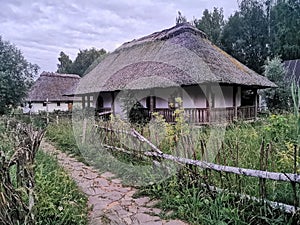 An old wooden Ukrainian hut on a farm in the evening, cloudy sky