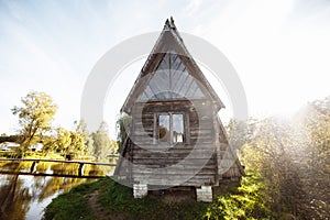 An old wooden village house stands on the edge of the forest by the lake against the blue sky. Old village hut. Peasant