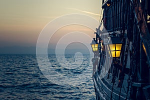 Old wooden vintage pirate ship on sea water surface in sunset evening romantic time with yellow light from soft focus lantern in