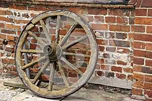 Old wooden wagon wheel in front of a brick wall.