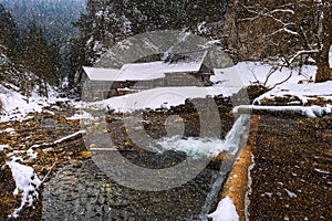 Old wooden water mill in winter with snow falling