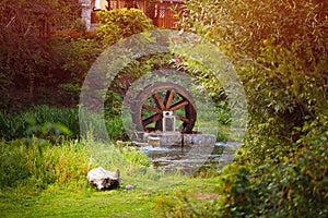 Old wooden waterwheel watermill on a horse farm. The old water wheel covered with moss. Flowing water to the mill. Old technology