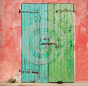 Old wooden weathered door painted on one side of turquoise and on the other green, with rusty lock and padlock. Pink wall peeled a