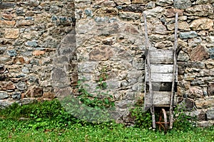 Old wooden wheelbarrow leaned against a stone wall