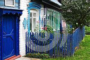 Old wooden and white brick house with green carved window frames, blue door and front garden fence