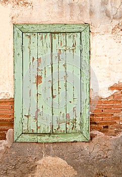 Old wooden window with green shutters on weathered wall.