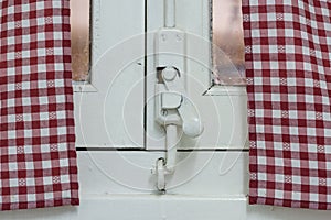 Old wooden window lock, painted covering wood, metal and screws. Vintage curtain with grid pattern