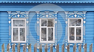 Old wooden windows with carved architraves. Blue facade of typical rural Russian house.