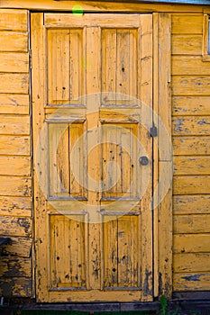 Old wooden yellow weathered textured wall with a door in the village. Hot sunny summer day