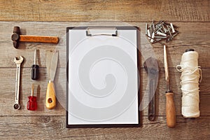 Old work tools on wooden background with blank notepad. View from above.