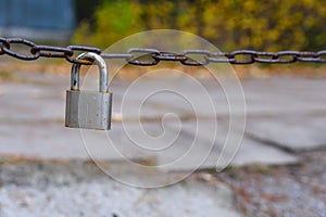 Old and worn chrome padlock hangs on the rusty chain. Chain protects the entrance to the boat station. Green bushes on the