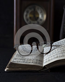 Old worn Glasses resting on an opened book with books and clock in background