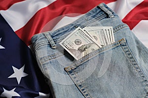 Old worn jeans are lying on flag United States America and there are hundred dollar bills in pocket