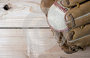 Old worn leather baseball glove and used ball on a wooden