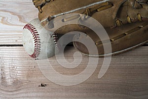 Old worn leather baseball glove and used ball on a wooden