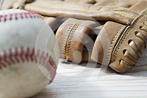 Old worn leather baseball glove and used ball on a wooden table