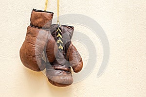 Old worn leather brown boxing gloves hang against the background of the wall in yellow.