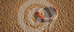 Old worn lifebuoy lying in rippled sand of beach.