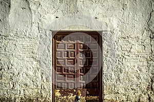 Old and worn maroon double wooden door with a lock on a whitewashed wall very textured photo