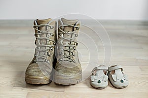 Old worn military boots and baby shoes on wooden floor. Concept of military father and family