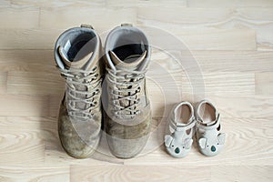 Old worn military boots and baby shoes on wooden floor. Concept of military father and family