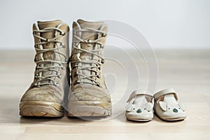 Old worn military boots and baby shoes on wooden floor. Concept of military father and family