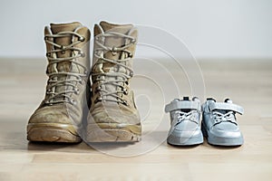 Old worn military boots and baby shoes on wooden floor. Concept of military father and family