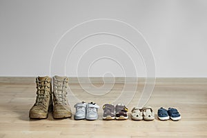 Old worn military boots and lot of baby shoes on wooden floor. Military father and family concept