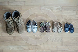 Old worn military boots and lot of baby shoes on wooden floor. Military father and family concept