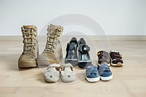Old worn military boots, women`s shoes and lot of baby shoes on wooden floor
