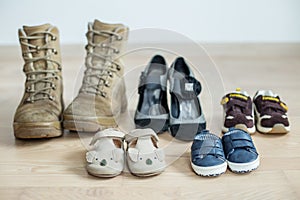 Old worn military boots, women`s shoes and lot of baby shoes on wooden floor