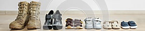 Old worn military boots, women`s shoes and lot of baby shoes on wooden floor. Banner for web site