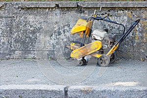 An old worn-out gasoline cutter stands against a concrete wall