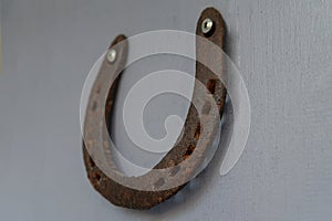 An old worn-out and rusty metal horseshoe nailed to the light grey wooden door of a village house. Horseshoe is a sign of fortune