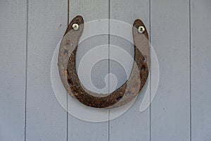 An old worn-out and rusty metal horseshoe nailed to the light lilac wooden door of a village house. Horseshoe is a sign of fortune