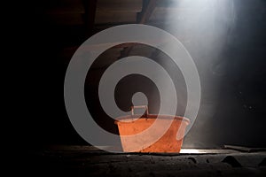 Old worn red bucket standing in a foggy environment on the attic. Red bucket lit by a ray of light from the attic window