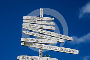 Old worn and weathered wooden sign post pointing in multiple different directions with blue sky background.