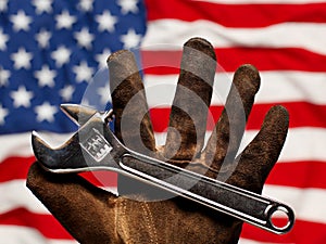 Old and worn work glove holdng adjustable wrench over US American flag,. American labor, work, and employment concept