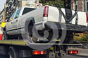 Old wrecked broken pickup vehicle accident transportation on flatbed tow truck machine on city street. Emergency road