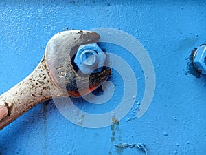 Old wrench is tightening the nut on the blue metal plate. Corroded and rusty Spanner