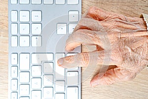 Old wrinkled hand of aged human on the computer keyboard