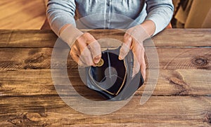 Old wrinkled hand holding coin, empty wallet, wooden background.