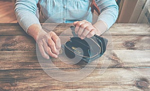 Old wrinkled hand holding coin, empty wallet, wooden background.