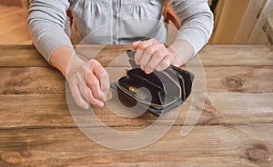 Old wrinkled hand holding coin, empty wallet, wooden background.