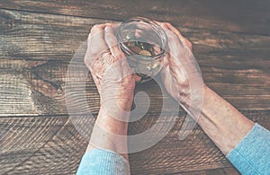 Old wrinkled hands holding jar with coins, wooden background.