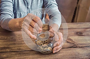 Old wrinkled hands holding jar with coins, wooden background.