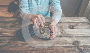 Old wrinkled hands holding jar with coins, wooden background.